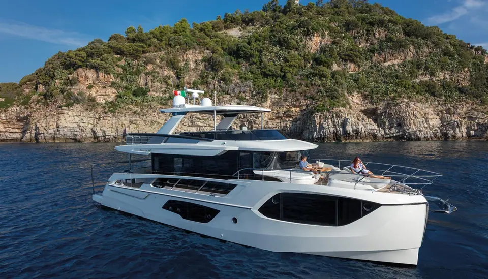 Absolute Navetta 64 cruising slowly past a rocky green headland
