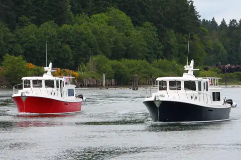 Two American Tug 365 cruisers, one red and one navy, running together in a wooded channel