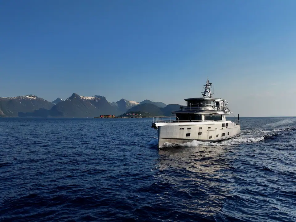 Arksen 85 cruising past snowy mountains with its tall wheelhouse and aft deck in view