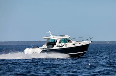 Back Cove 34O cruising past a shoreline, seen from astern with its outboards visible
