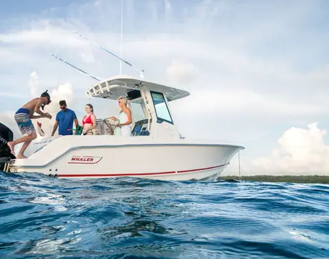 Boston Whaler 250 Outrage at anchor in profile with a family aboard