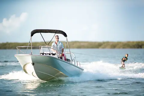 Boston Whaler 170 Montauk with a bimini top towing a wakeboarder