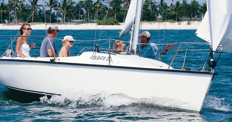 Colgate 26 reaching off a palm lined beach with a family aboard