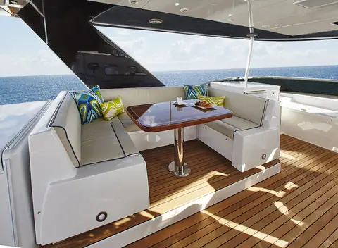 Hatteras 70 Motor Yacht flybridge dining area with a varnished table and white settees