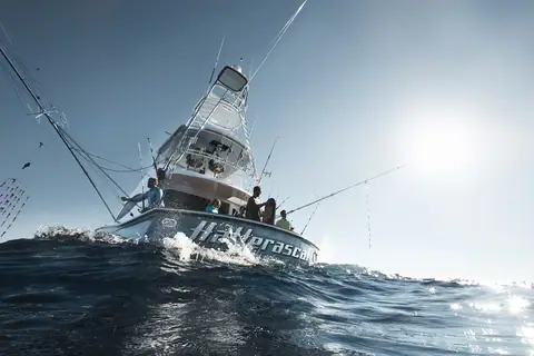 Hatteras GT59 underway from a low angle with anglers aboard and its tuna tower and outriggers