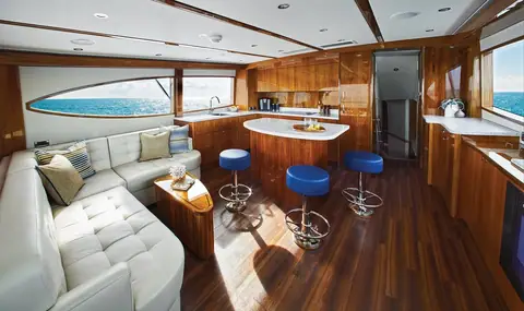 Hatteras GT59 salon with a white leather settee, teak sole and a galley bar with blue stools