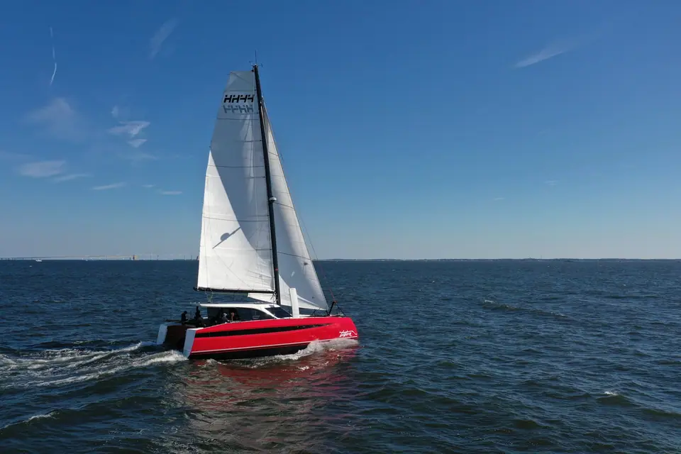 HH44 catamaran with a red hull sailing under main and jib on open water