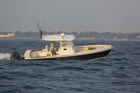 Hunt 32 Center Console running in profile with its T top, rod holders and twin outboards
