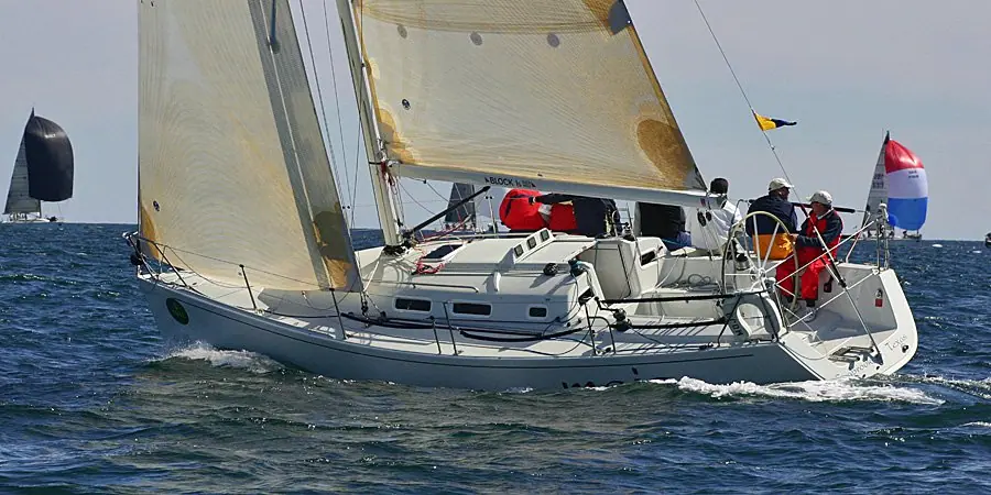 J/109 sailing upwind with crew in the cockpit and a flag flying from the backstay
