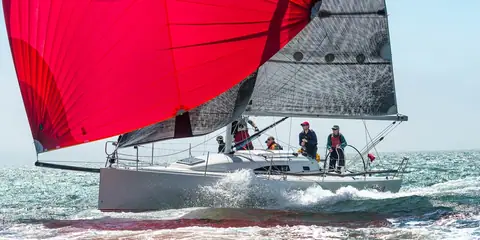 J/111 reaching fast under a red asymmetric spinnaker with crew aft