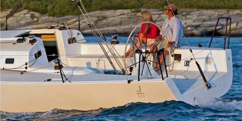 J/111 open cockpit with twin wheels and two people sailing near a rocky shore