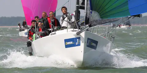 J/88 racing downwind bow on with crew gathered in the cockpit