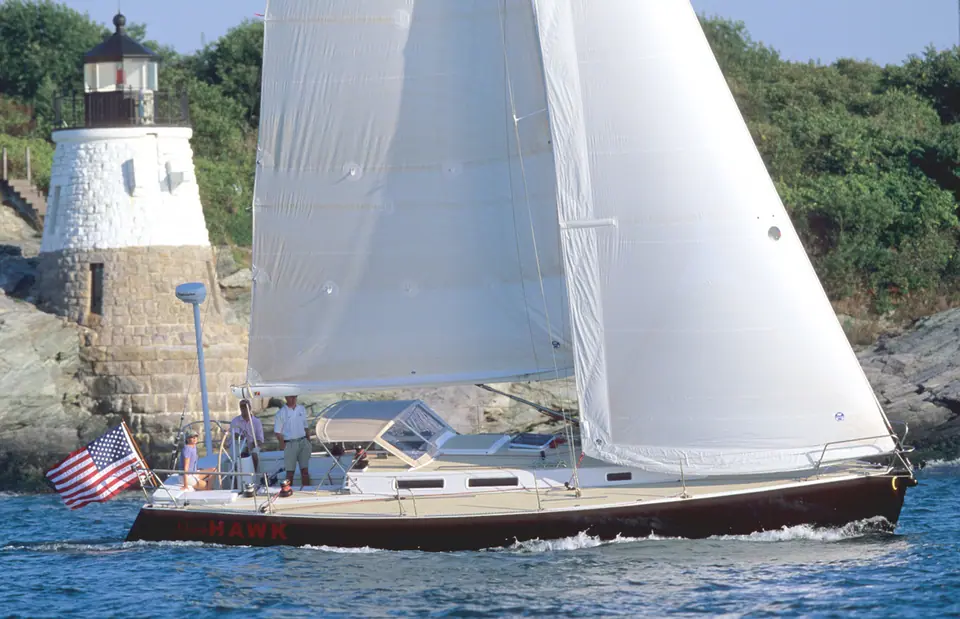 J/120 sailing under main and genoa past a stone lighthouse with crew in the cockpit