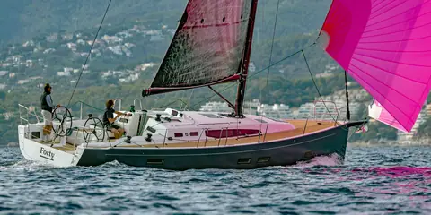 J/40 reaching under a pink asymmetric spinnaker along a wooded shore