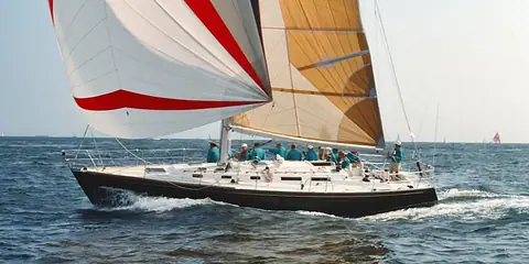 Dark hulled J/44 reaching under a red and white spinnaker with crew aboard