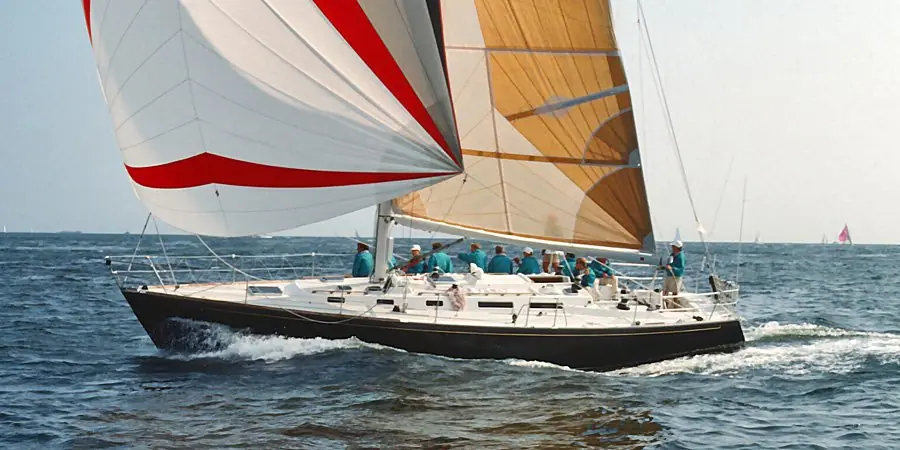 Dark hulled J/44 reaching under a red and white spinnaker with crew aboard