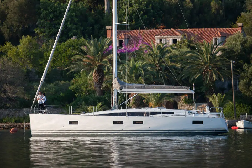 Jeanneau 54 at anchor in profile off a palm lined shore with a couple on the bow
