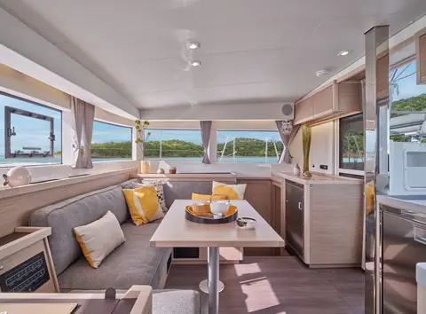 Lagoon 40 saloon with a gray settee, dining table and galley under wraparound windows