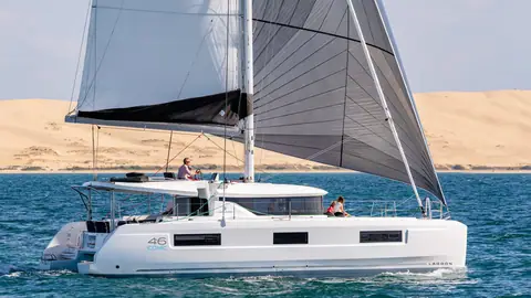 Lagoon 46 catamaran sailing in profile past a sand dune under mainsail and jib