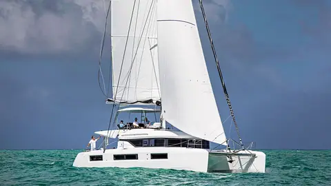 Lagoon 50 flybridge catamaran sailing toward the camera under full main and genoa with crew aboard
