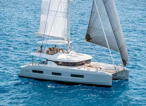 Lagoon 55 catamaran sailing on blue water under mainsail and genoa with guests on the flybridge