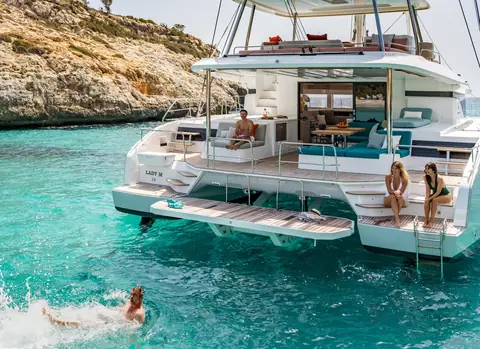 Lagoon 55 at anchor in a turquoise cove seen from astern with swimmers off the transom steps