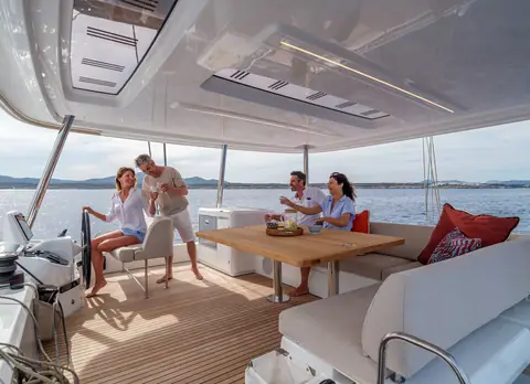Lagoon 55 aft cockpit with a teak table, sofa and guests under the flybridge overhang