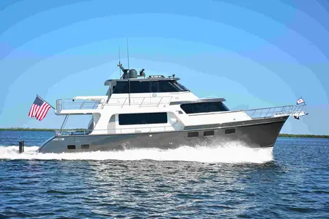 Marlow Explorer 58E with a gray hull cruising past a green shoreline, flybridge and long range profile visible