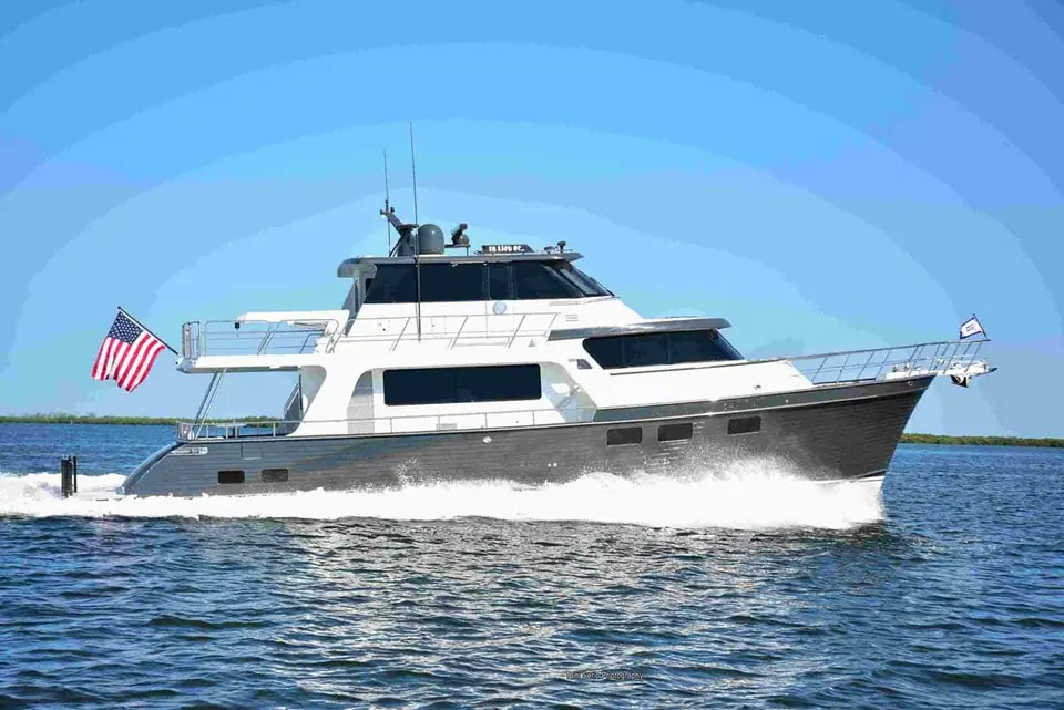 Marlow Explorer 58E with a gray hull cruising past a green shoreline, flybridge and long range profile visible