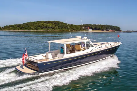 MJM 50z with a dark blue hull cruising past a wooded island, seen from the port quarter
