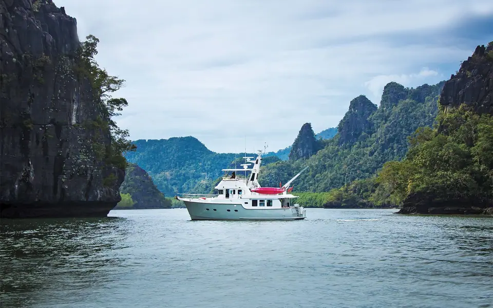 Nordhavn 47 with a gray hull at anchor below limestone cliffs, kayak on the boat deck