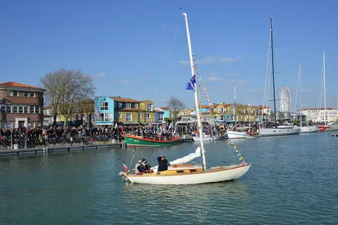 Wooden Nordic Folkboat motoring through a crowded harbor in La Rochelle