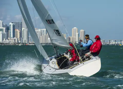 Sonar heeled hard upwind off a city skyline with crew on the rail