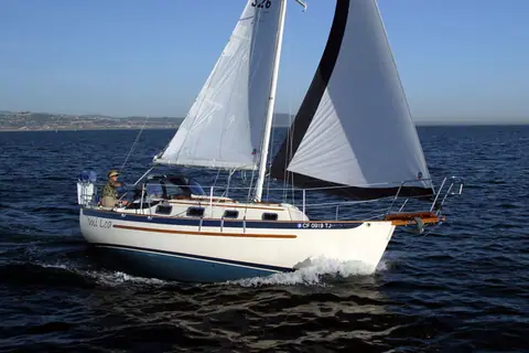 Pacific Seacraft Dana 24 sailing in profile under main and jib along a rocky coast