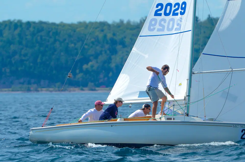 Ensign keelboat sailing upwind with a white hull and crew trimming sails