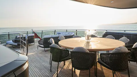Princess X95 sun deck with a round dining table and woven chairs in low evening sun