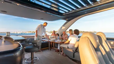 Princess Y85 flybridge with guests dining at a table beside the helm under the hardtop
