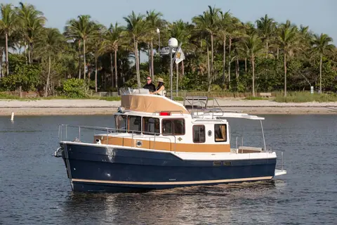 Ranger Tugs R-31 CB with a navy hull and flybridge cruising in profile off a palm lined beach