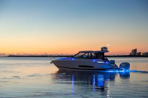Regal 36 XO idling at dusk with blue underwater lights and the twin outboards lit