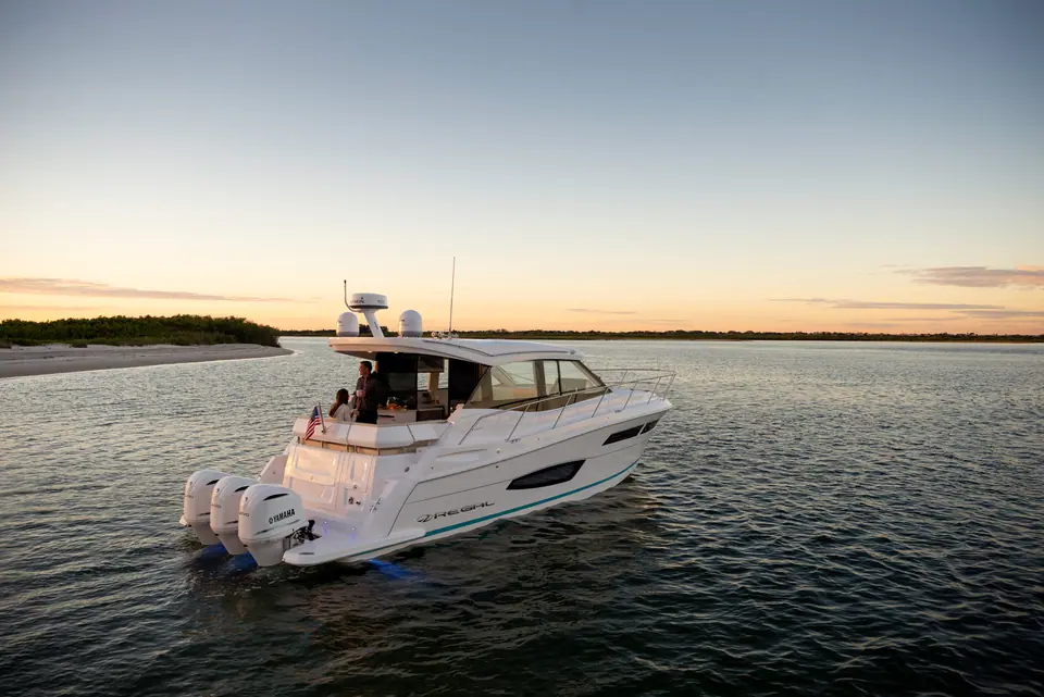 Regal 38 XO seen from astern with triple outboards and guests in the cockpit at dusk