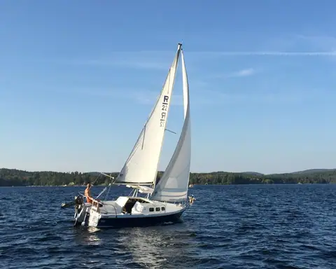 Rhodes 22 sailing on a lake under main and genoa with R22 sail insignia and an outboard on the transom