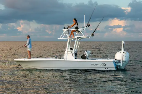 Robalo 246 Cayman SD in profile at sunset with an angler on the bow and a woman on the Sky Deck