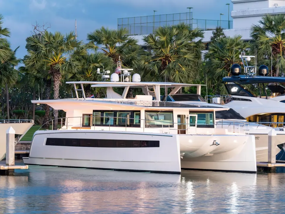 Silent 60 catamaran moored in a marina seen in profile with palm trees behind
