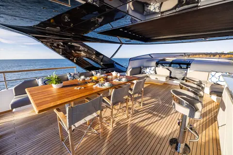 Sunseeker 100 Yacht flybridge with a teak dining table, bar stools and hardtop overhead