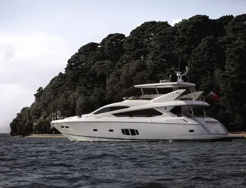Sunseeker 80 Yacht at anchor in profile below a wooded headland