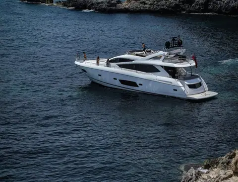 Sunseeker Manhattan 73 at anchor in a rocky cove with guests on the flybridge and foredeck