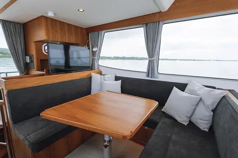 Targa 41 wheelhouse dinette with teak table, gray upholstery, TV cabinet and large side windows