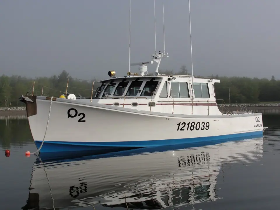White Wesmac 42 Q2 with a long house and blue boot stripe moored on a calm bay