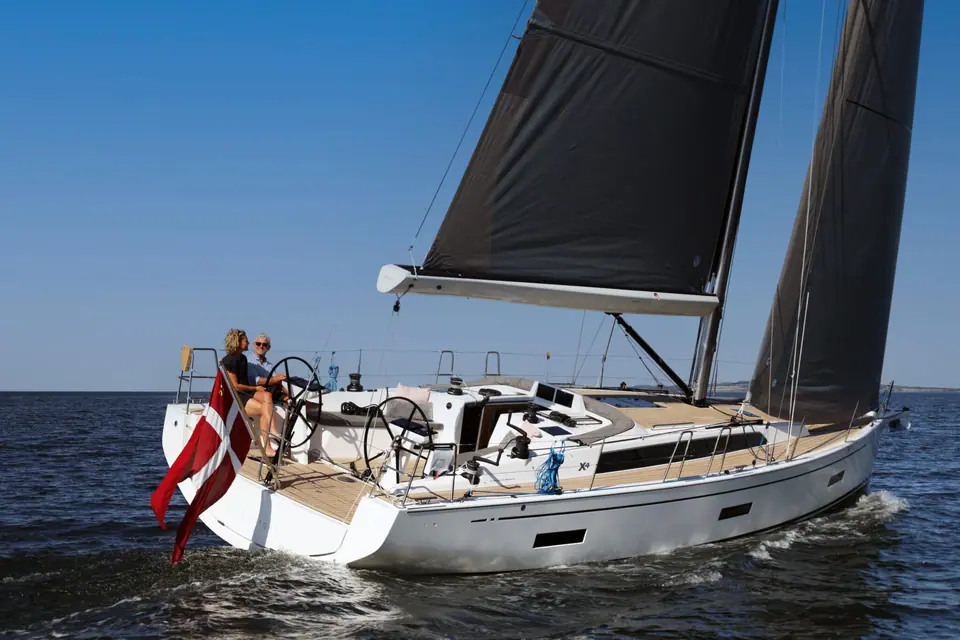 X Yachts X4.3 heeling under dark sails with crew at the twin wheels and a Danish ensign